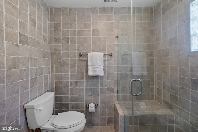 bathroom featuring tile walls, a shower with shower door, and toilet