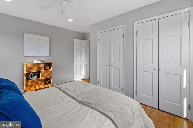 bedroom with ceiling fan, light hardwood / wood-style flooring, and two closets