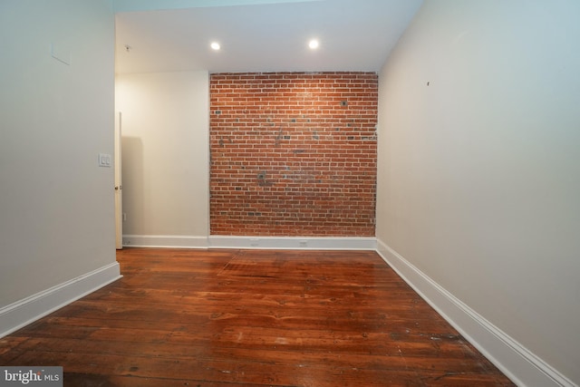 spare room with brick wall and dark hardwood / wood-style flooring