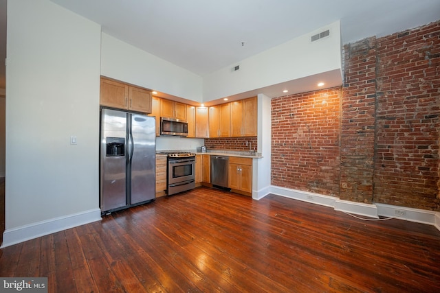 kitchen with stainless steel appliances, brick wall, dark hardwood / wood-style floors, and a towering ceiling