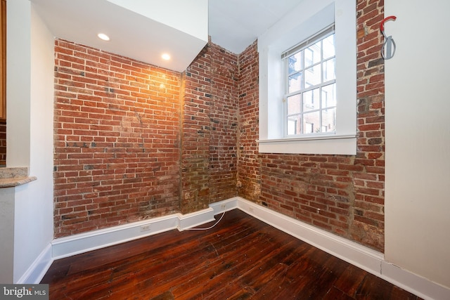 empty room with hardwood / wood-style flooring and brick wall