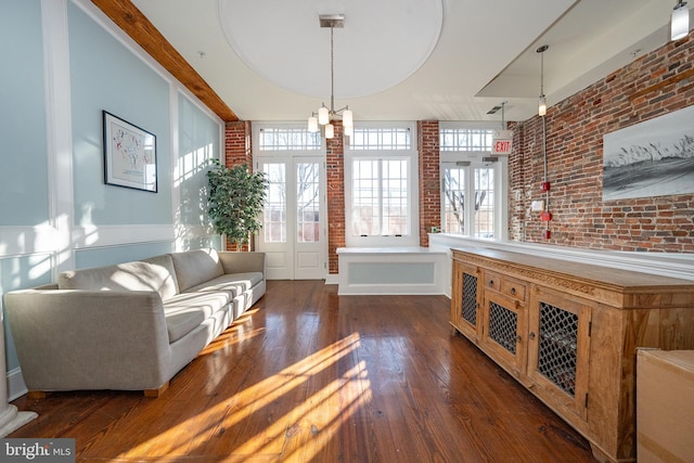 living area with dark hardwood / wood-style flooring, an inviting chandelier, and brick wall