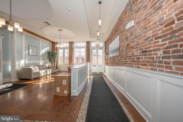 hall featuring dark wood-type flooring, a chandelier, and brick wall