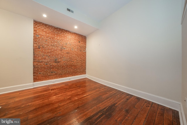 spare room featuring wood-type flooring and brick wall