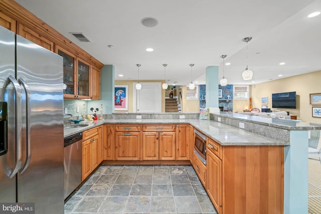 kitchen featuring appliances with stainless steel finishes, backsplash, light stone countertops, decorative light fixtures, and kitchen peninsula