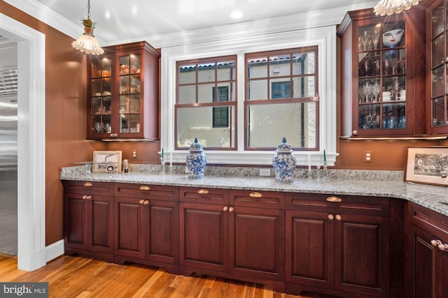 bar with pendant lighting, crown molding, light stone countertops, and light hardwood / wood-style floors