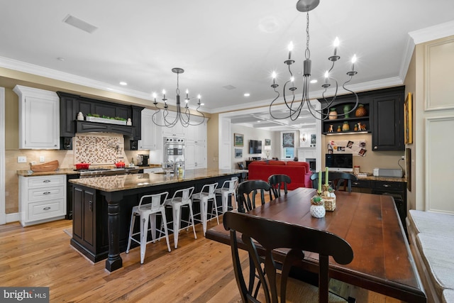 kitchen with stone countertops, white cabinets, a kitchen breakfast bar, a large island with sink, and light hardwood / wood-style floors