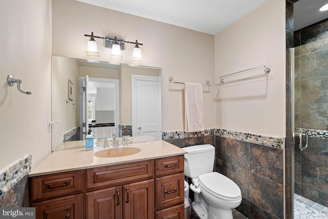 bathroom featuring toilet, tile walls, vanity, and a shower with shower door