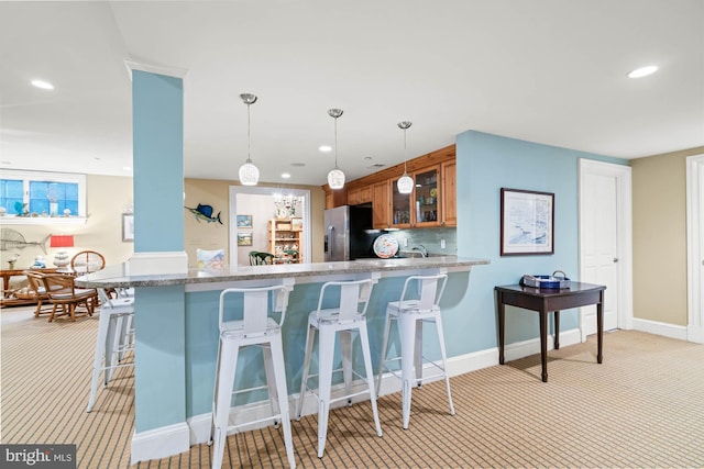 kitchen with pendant lighting, kitchen peninsula, a kitchen breakfast bar, light colored carpet, and stainless steel fridge with ice dispenser