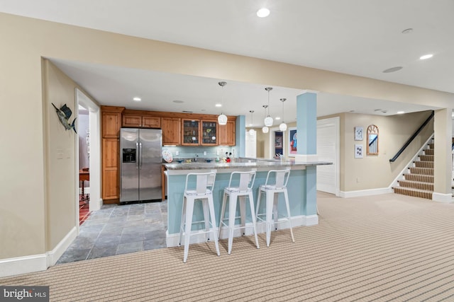 kitchen featuring a breakfast bar, hanging light fixtures, tasteful backsplash, stainless steel fridge with ice dispenser, and kitchen peninsula