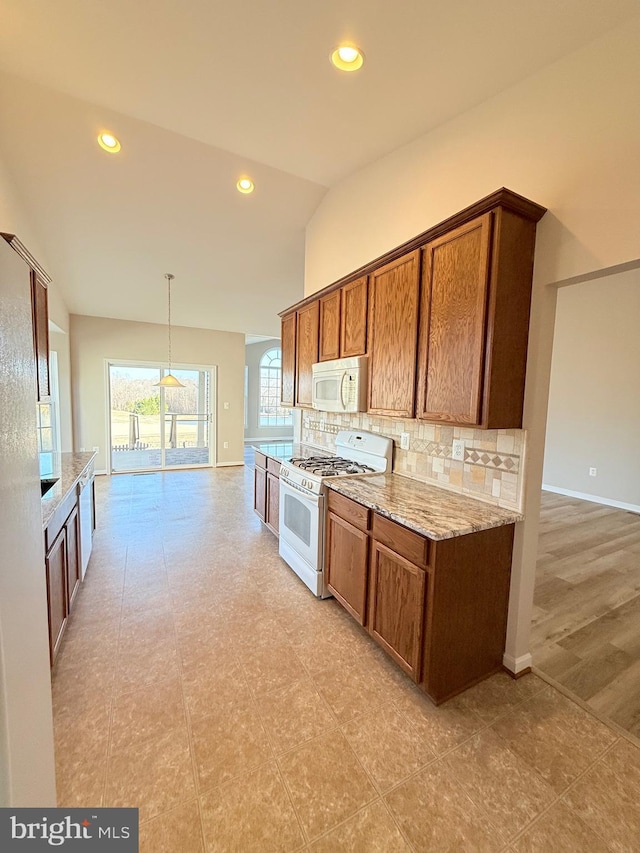 kitchen featuring lofted ceiling, white appliances, hanging light fixtures, light stone countertops, and decorative backsplash