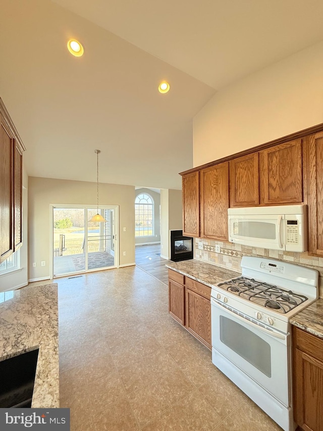 kitchen featuring lofted ceiling, light stone counters, hanging light fixtures, white appliances, and decorative backsplash