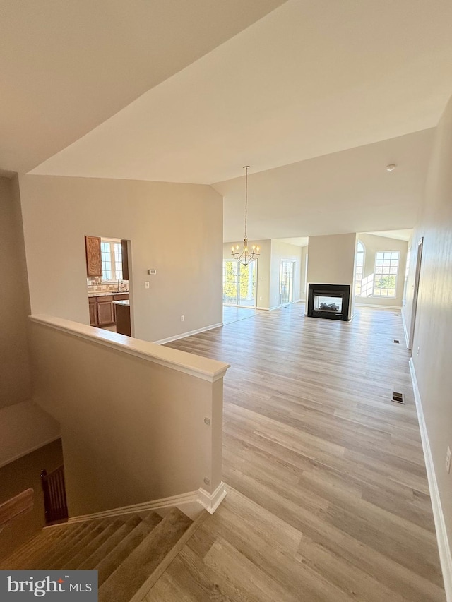 interior space featuring a notable chandelier, plenty of natural light, wood-type flooring, and vaulted ceiling