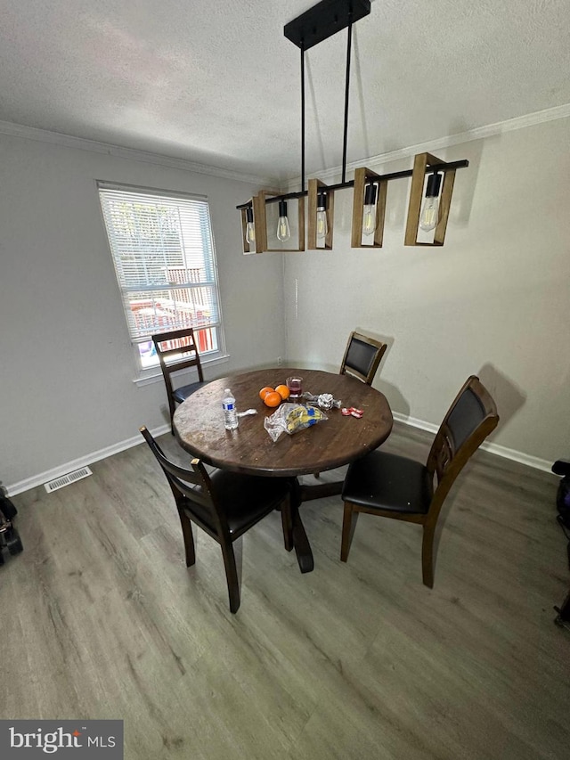 dining area featuring wood-type flooring, ornamental molding, and a textured ceiling