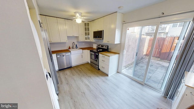 kitchen featuring appliances with stainless steel finishes, butcher block countertops, white cabinetry, sink, and light wood-type flooring