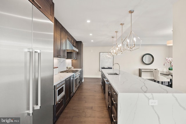 kitchen featuring dark brown cabinetry, sink, decorative light fixtures, stainless steel appliances, and light stone countertops