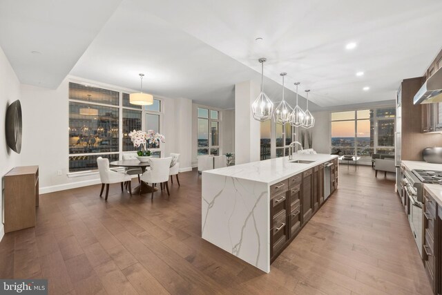 kitchen featuring decorative light fixtures, sink, expansive windows, a large island with sink, and light stone countertops