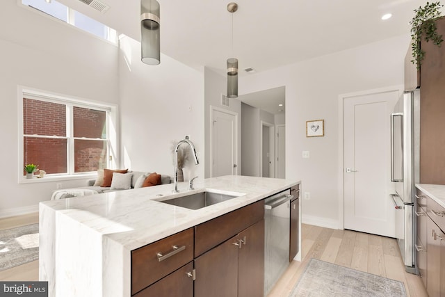 kitchen featuring sink, light stone counters, light hardwood / wood-style floors, stainless steel appliances, and a center island with sink