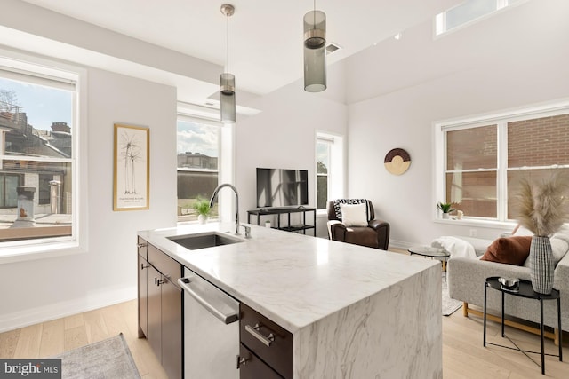 kitchen with pendant lighting, dishwasher, sink, a kitchen island with sink, and light hardwood / wood-style flooring