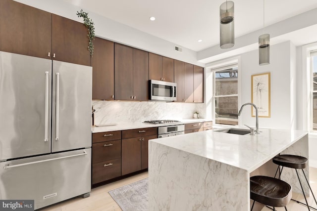 kitchen with sink, a breakfast bar, appliances with stainless steel finishes, hanging light fixtures, and decorative backsplash