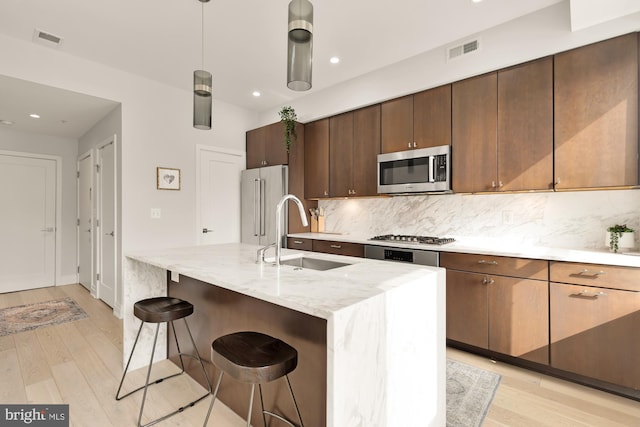 kitchen featuring sink, a breakfast bar, a kitchen island with sink, stainless steel appliances, and decorative backsplash