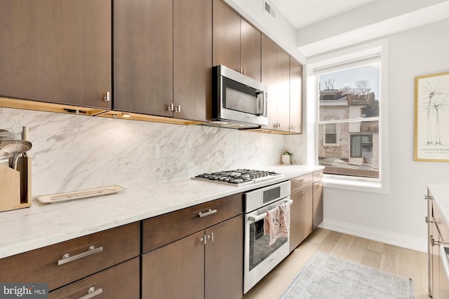 kitchen featuring tasteful backsplash, dark brown cabinetry, stainless steel appliances, light stone countertops, and light wood-type flooring