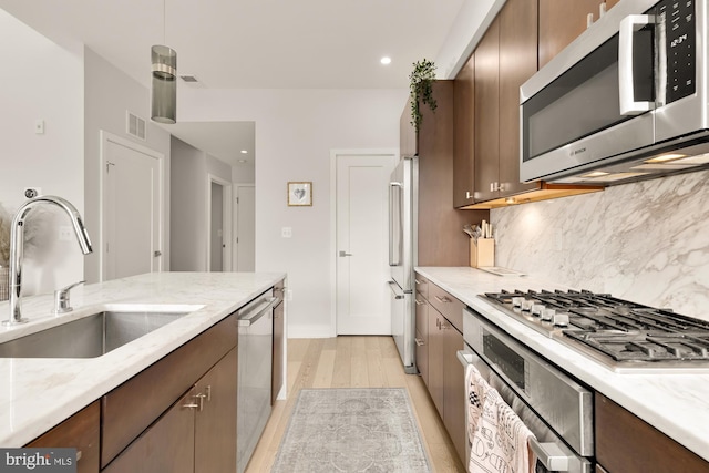 kitchen featuring dark brown cabinetry, sink, tasteful backsplash, stainless steel appliances, and light hardwood / wood-style floors