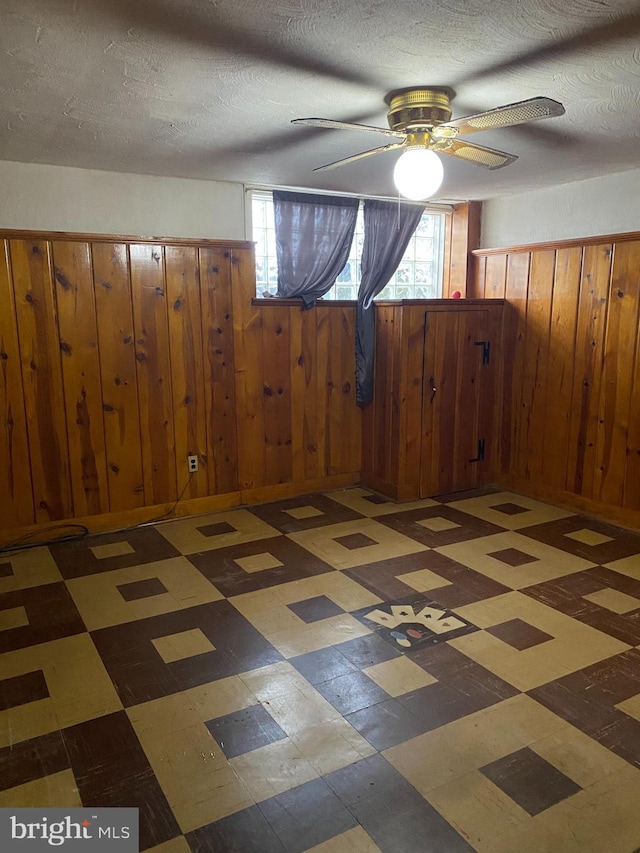 interior space featuring ceiling fan, a textured ceiling, and wood walls