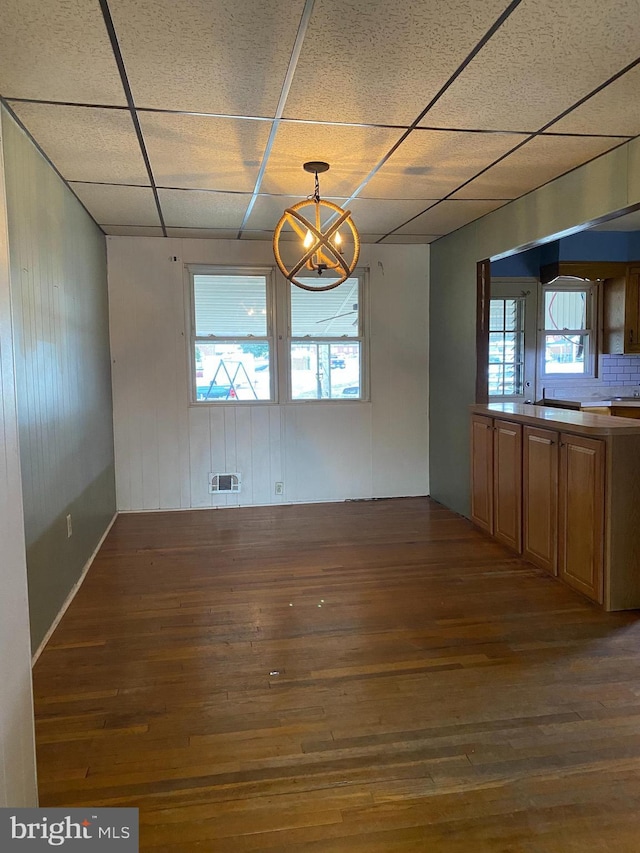 unfurnished dining area with a paneled ceiling, a notable chandelier, and dark hardwood / wood-style flooring