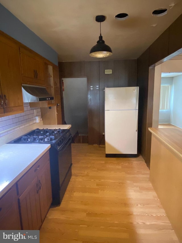 kitchen featuring light hardwood / wood-style flooring, black gas range, backsplash, white refrigerator, and decorative light fixtures