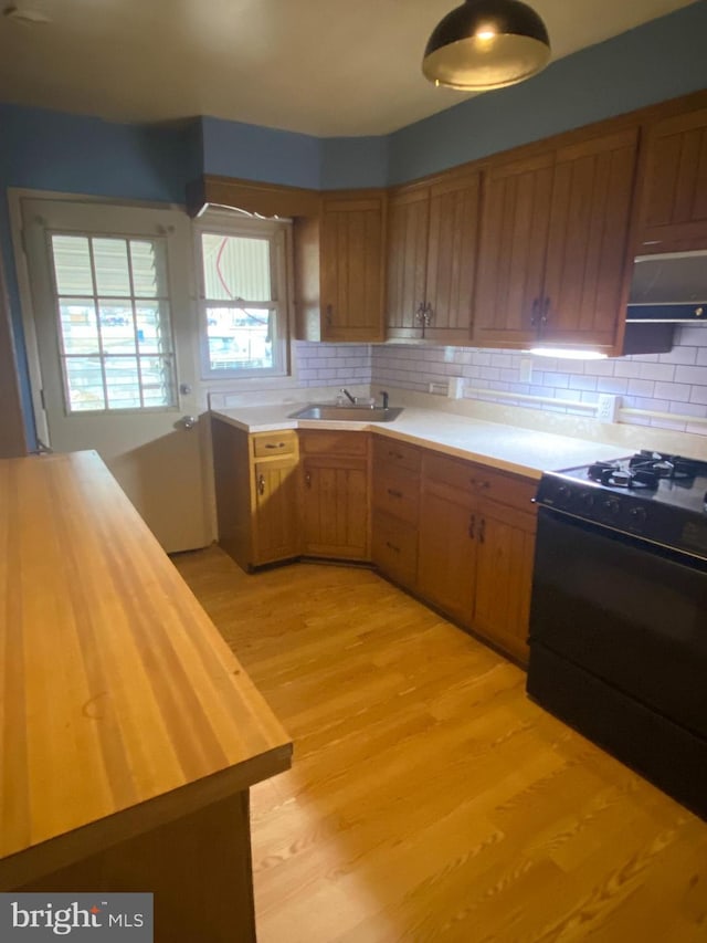 kitchen with butcher block counters, sink, ventilation hood, light wood-type flooring, and black gas range