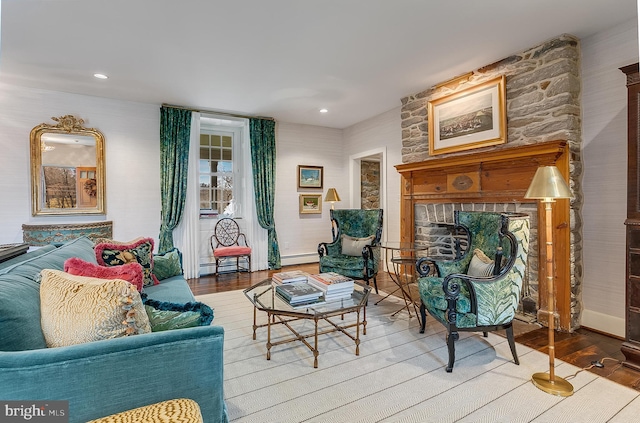 sitting room featuring wood-type flooring, a stone fireplace, and a baseboard heating unit