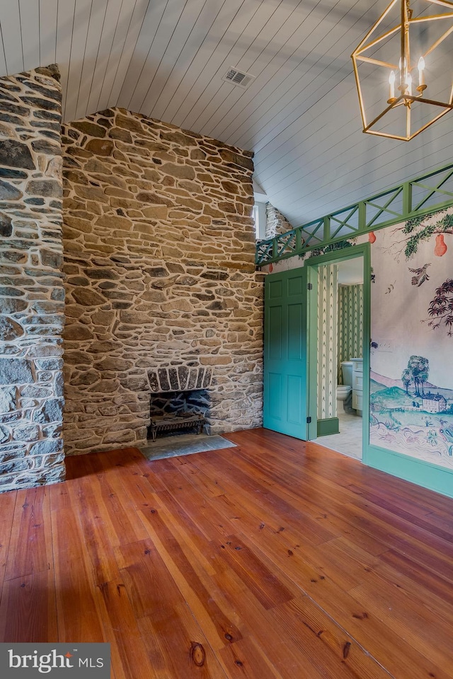 unfurnished living room featuring lofted ceiling, a stone fireplace, and hardwood / wood-style flooring