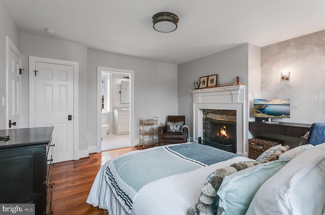 bedroom with a premium fireplace, ensuite bathroom, and dark hardwood / wood-style flooring