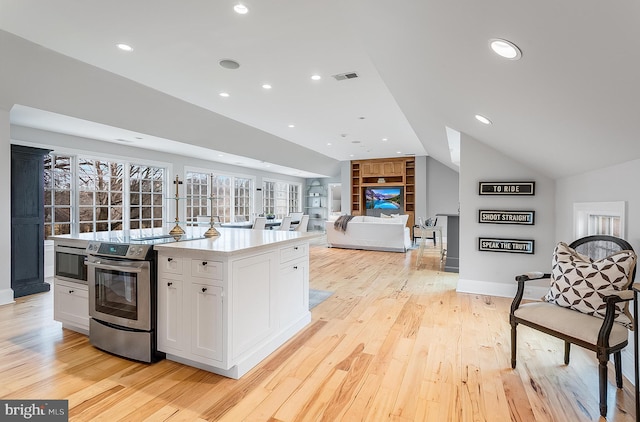 kitchen with appliances with stainless steel finishes, white cabinetry, lofted ceiling, a center island, and light wood-type flooring