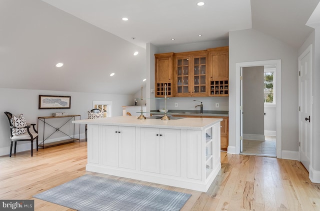 kitchen featuring lofted ceiling, sink, light hardwood / wood-style floors, and a kitchen island with sink