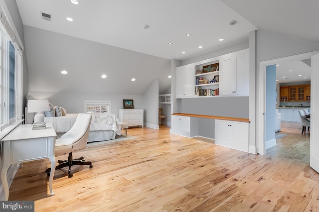 bedroom featuring built in desk, light hardwood / wood-style floors, and vaulted ceiling