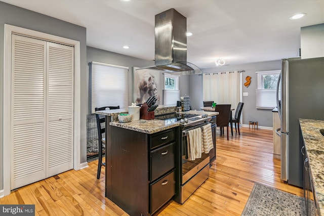 kitchen with light stone countertops, light wood-type flooring, stainless steel appliances, and island exhaust hood