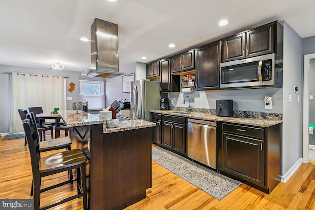 kitchen featuring a breakfast bar, appliances with stainless steel finishes, island range hood, light stone countertops, and a kitchen island