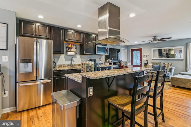 kitchen with a breakfast bar, sink, light hardwood / wood-style flooring, island exhaust hood, and stainless steel appliances