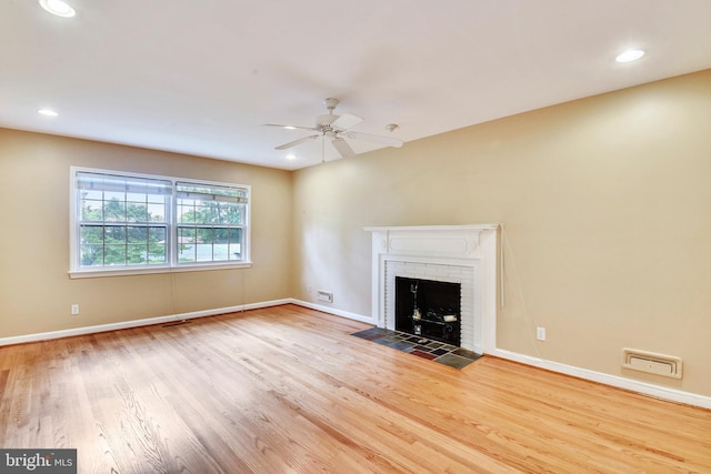 unfurnished living room with ceiling fan, a brick fireplace, and light hardwood / wood-style floors