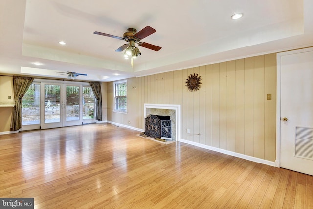 unfurnished living room featuring ceiling fan, a fireplace, a raised ceiling, and light hardwood / wood-style floors