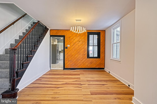 entryway with light wood-type flooring, an inviting chandelier, and wooden walls