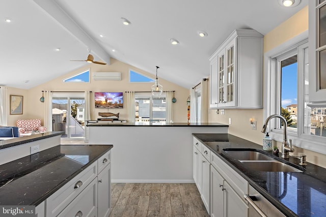 kitchen with white cabinetry, dark stone counters, a wall mounted AC, and sink