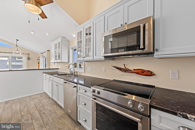 kitchen featuring appliances with stainless steel finishes, white cabinetry, lofted ceiling, sink, and light hardwood / wood-style flooring