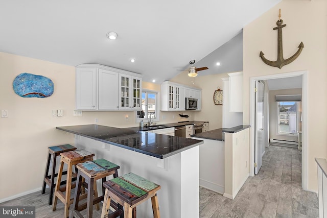 kitchen featuring white cabinetry, a breakfast bar area, kitchen peninsula, and vaulted ceiling