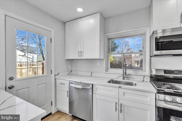 kitchen with stainless steel appliances, light stone countertops, sink, and white cabinets