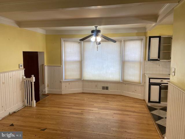 unfurnished dining area with beam ceiling, ornamental molding, ceiling fan, and light wood-type flooring