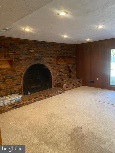 unfurnished living room featuring carpet flooring, a fireplace, a textured ceiling, and wood walls