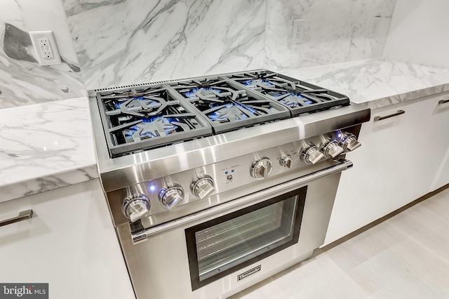 interior details featuring white cabinetry, tasteful backsplash, light stone counters, and high end stove